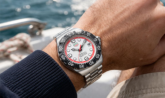Tag Heuer Formula 1 watch with white dial red accents and stainless steel bracelet on wrist by the sea